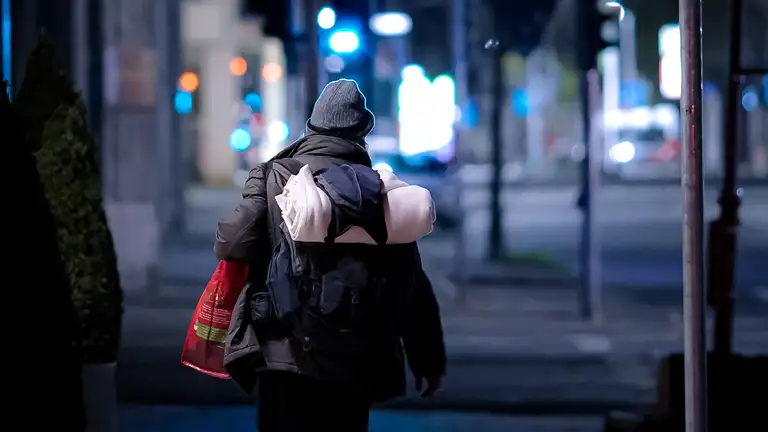 Person med rygsæk og bærepose går igennem bymiljø.